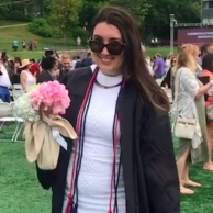 Morgan-Ann smiles at the camera while holding a bouquet and dressed in graduation robes. 