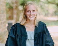 Madeline smiles at the camera while dressed in a graduation gown. 