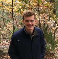 Miles grins up at the camera while hiking through a forest in the early fall.