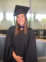 Zoe smiles at the camera while dressed in a black graduation cap and gown. 