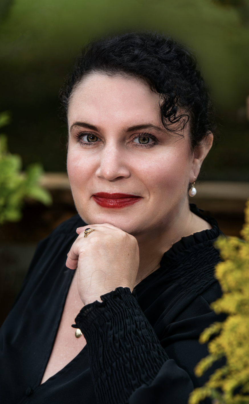 Jennifer Natalya Fink, a white woman with black hair, is pictured in a black blouse with her left hand under her chin.