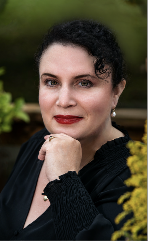 Jennifer Natalya Fink, a white woman with black hair, is pictured in a black blouse with her left hand under her chin.