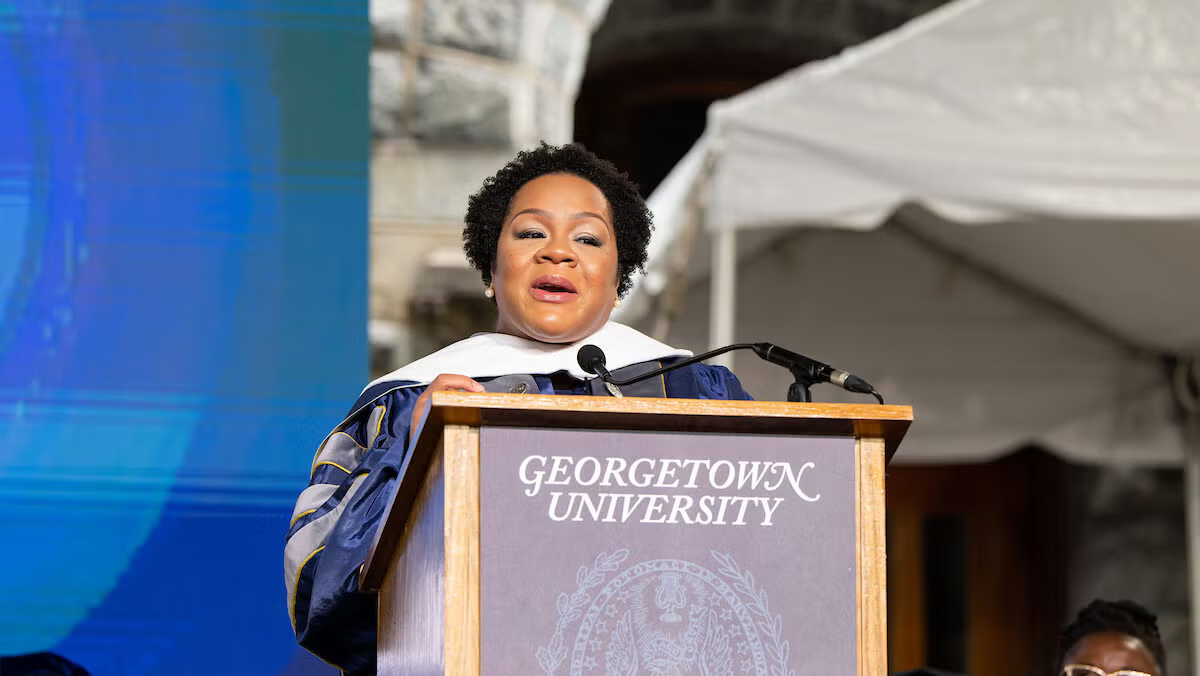 Yamiche Alcindor stands at a Georgetown University lectern in graduation regalia.