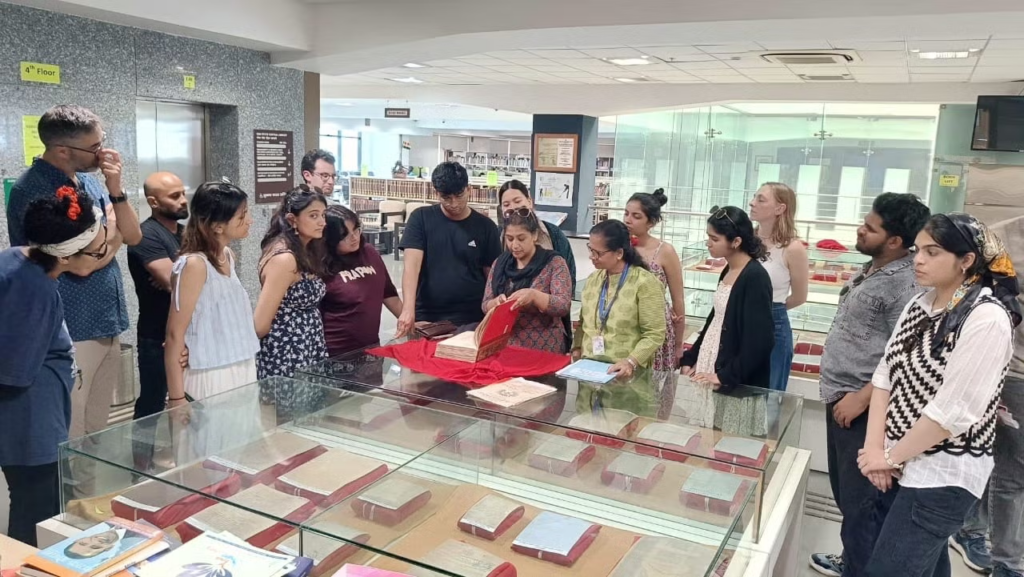 Students gather around a glass display case as an archivist explores an open tome on top of it.