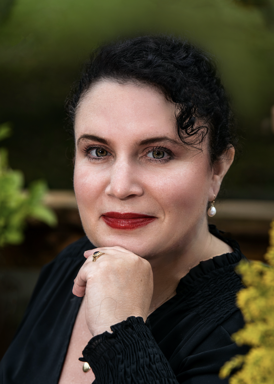 Jennifer Natalya Fink, a white woman with black hair, is pictured in a black blouse with her left hand under her chin.