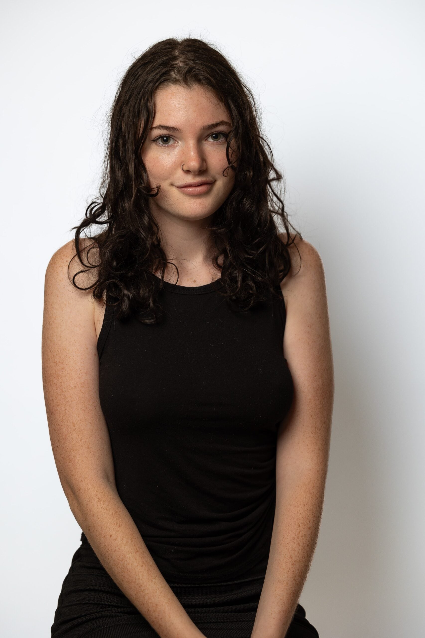Sydney stands in a black dress, against a white background, smiling softly at the viewer. 