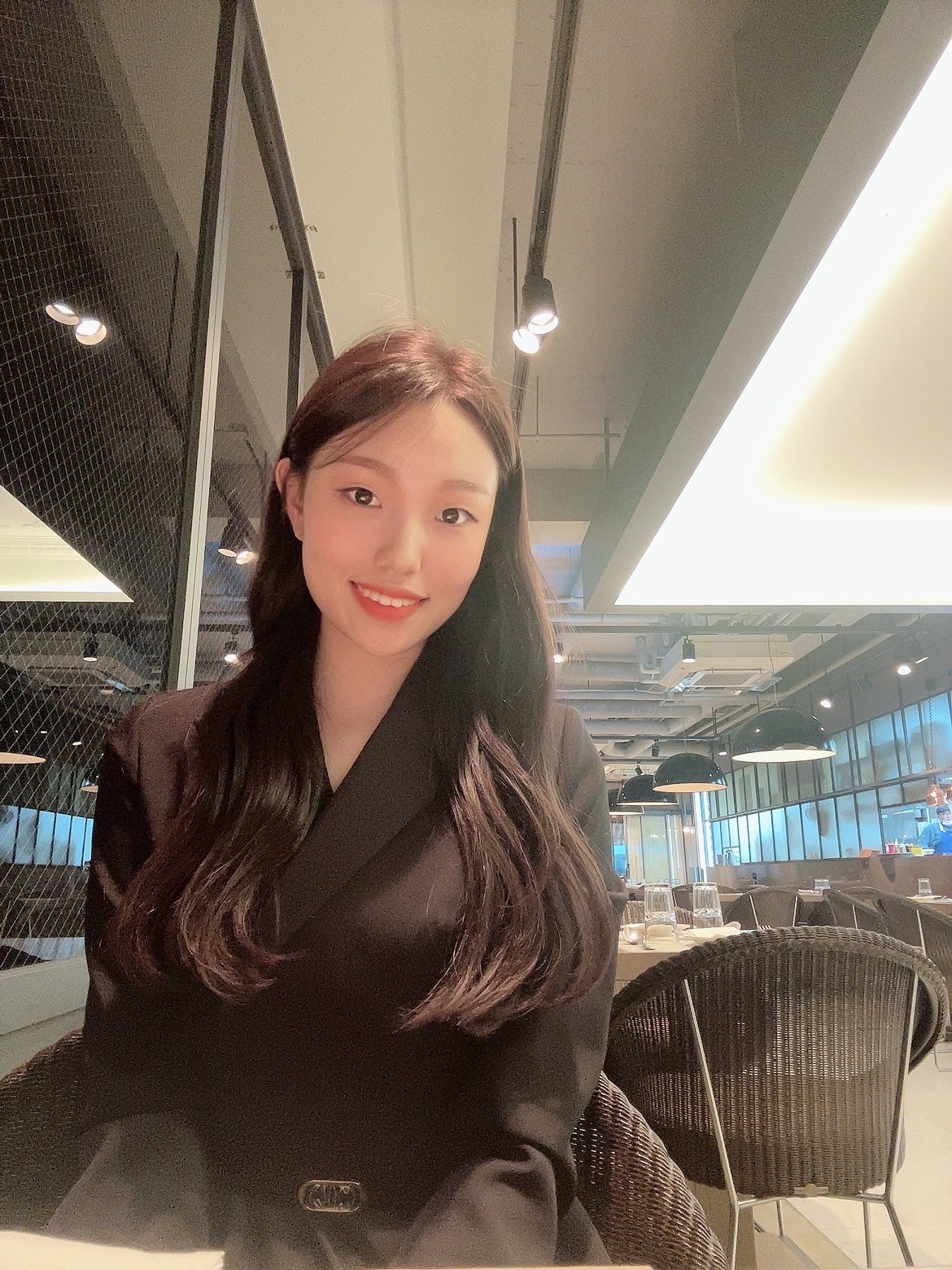 Seyoung sits in a brightly lit interior, wearing a simple black top and smiling at the viewer. 