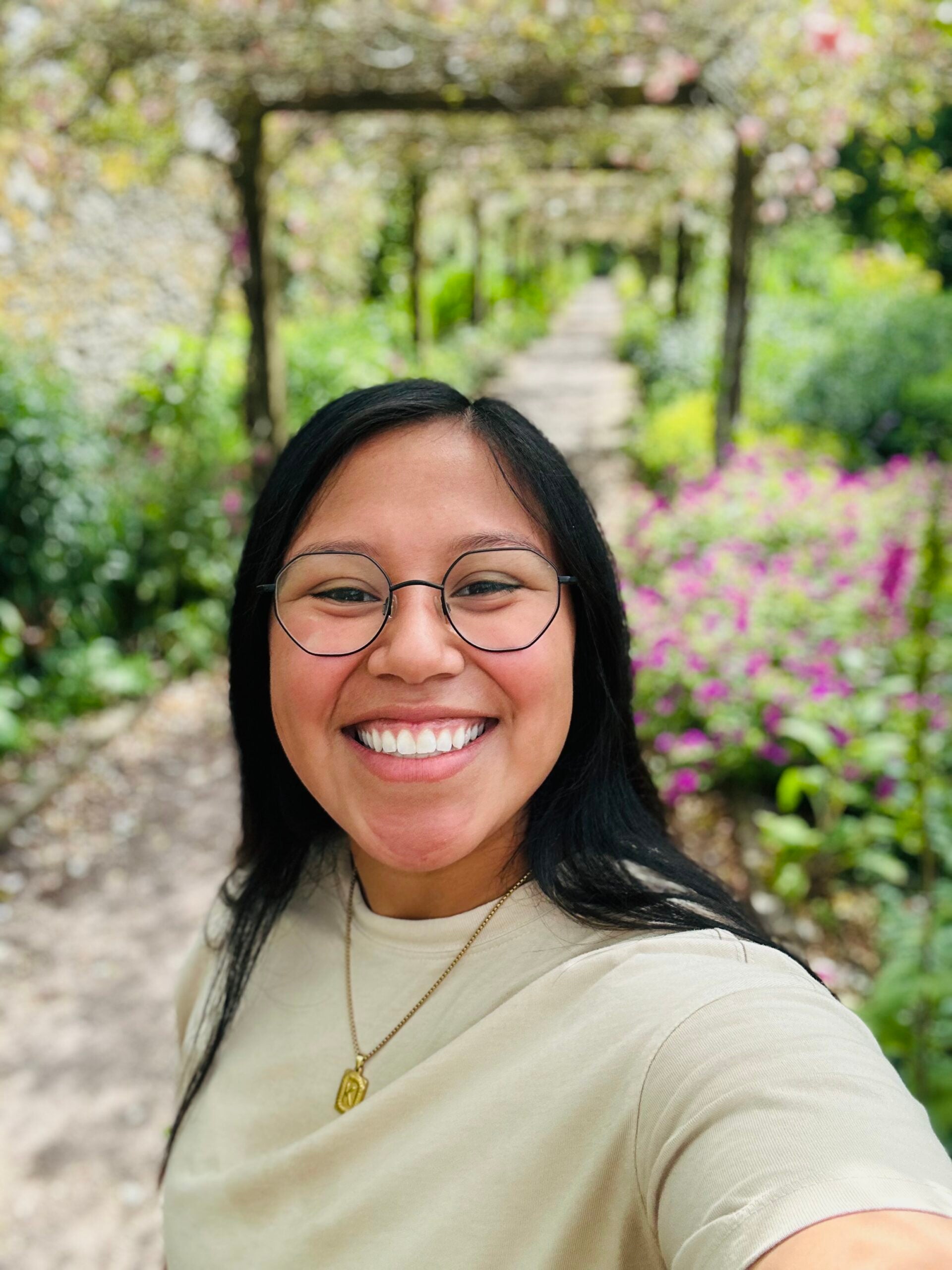 Kristina stands in a flowery background, smiling widely at the viewer. 