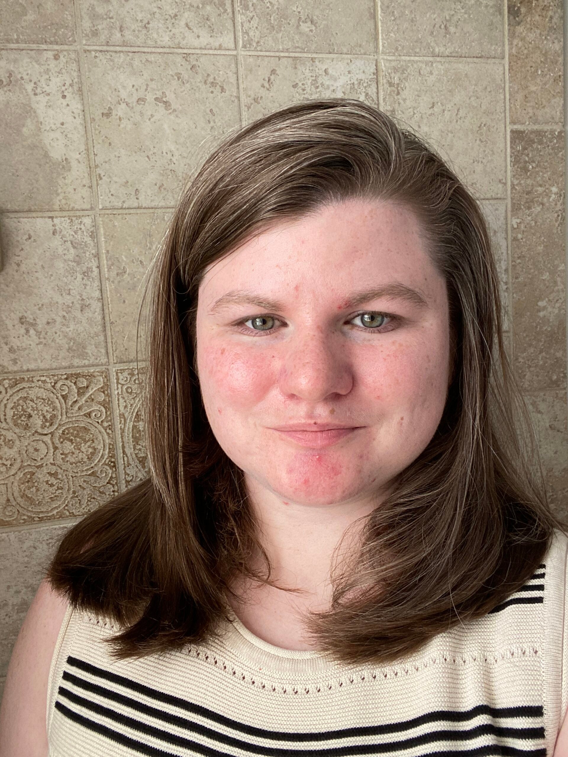 Gracelyn stands against a tiled background, wearing a striped top and smiles at the viewer