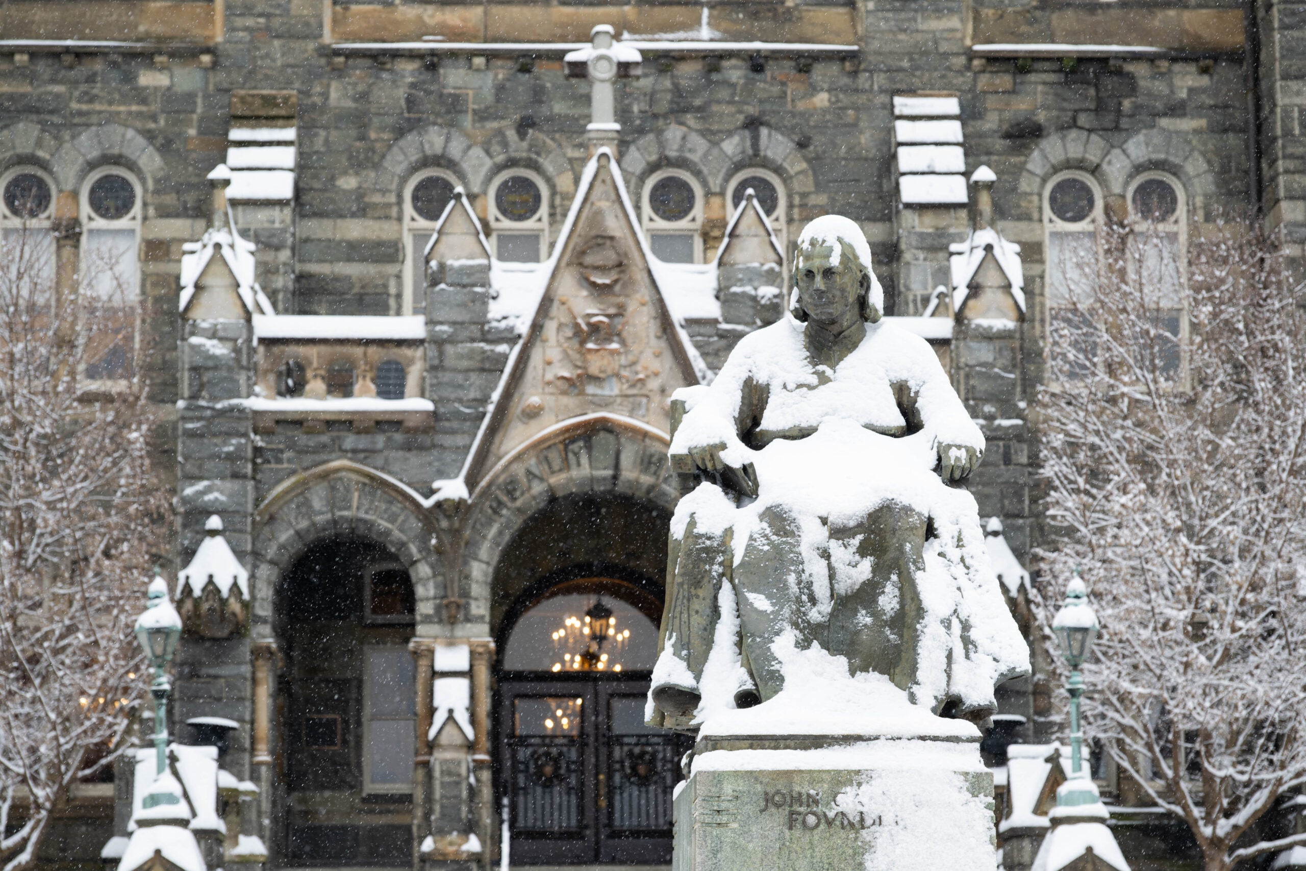A snowy photo of the grey-stone statue of Father John Carroll, founder of Georgetown University