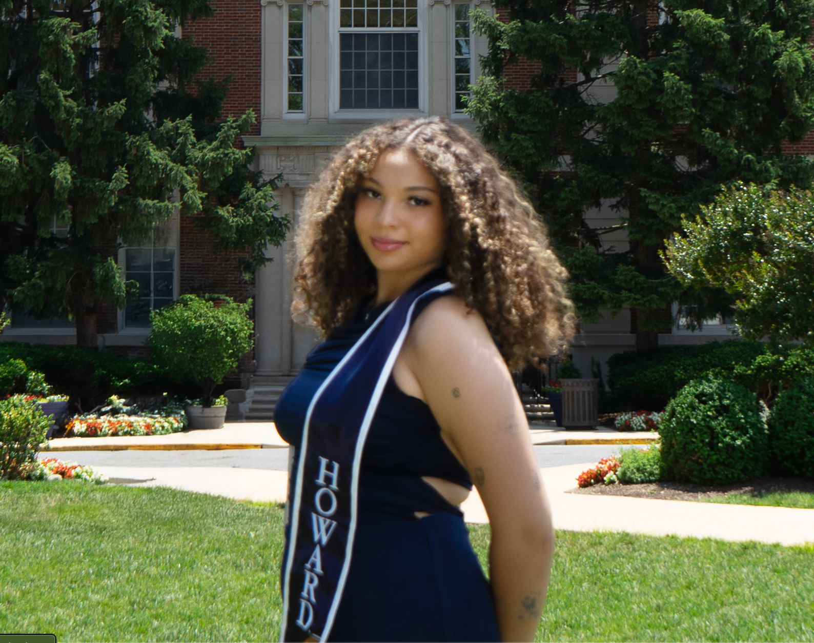 Sofia stands against a university background, wearing a stole and black dress, smiling and turning toward the viewer