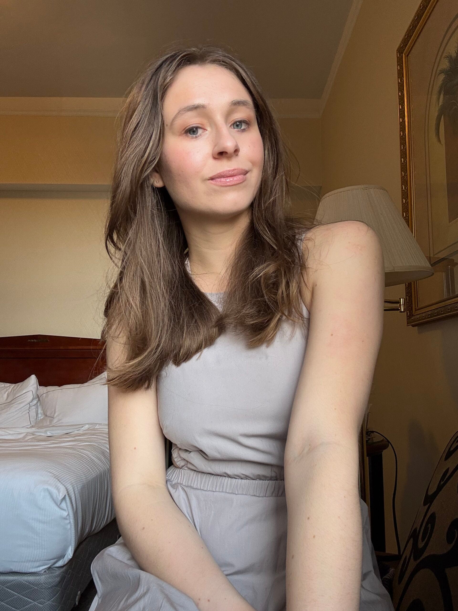 Lauren stands with her shoulders raised and head cocked to the side, smiling at the viewer with confidence. 