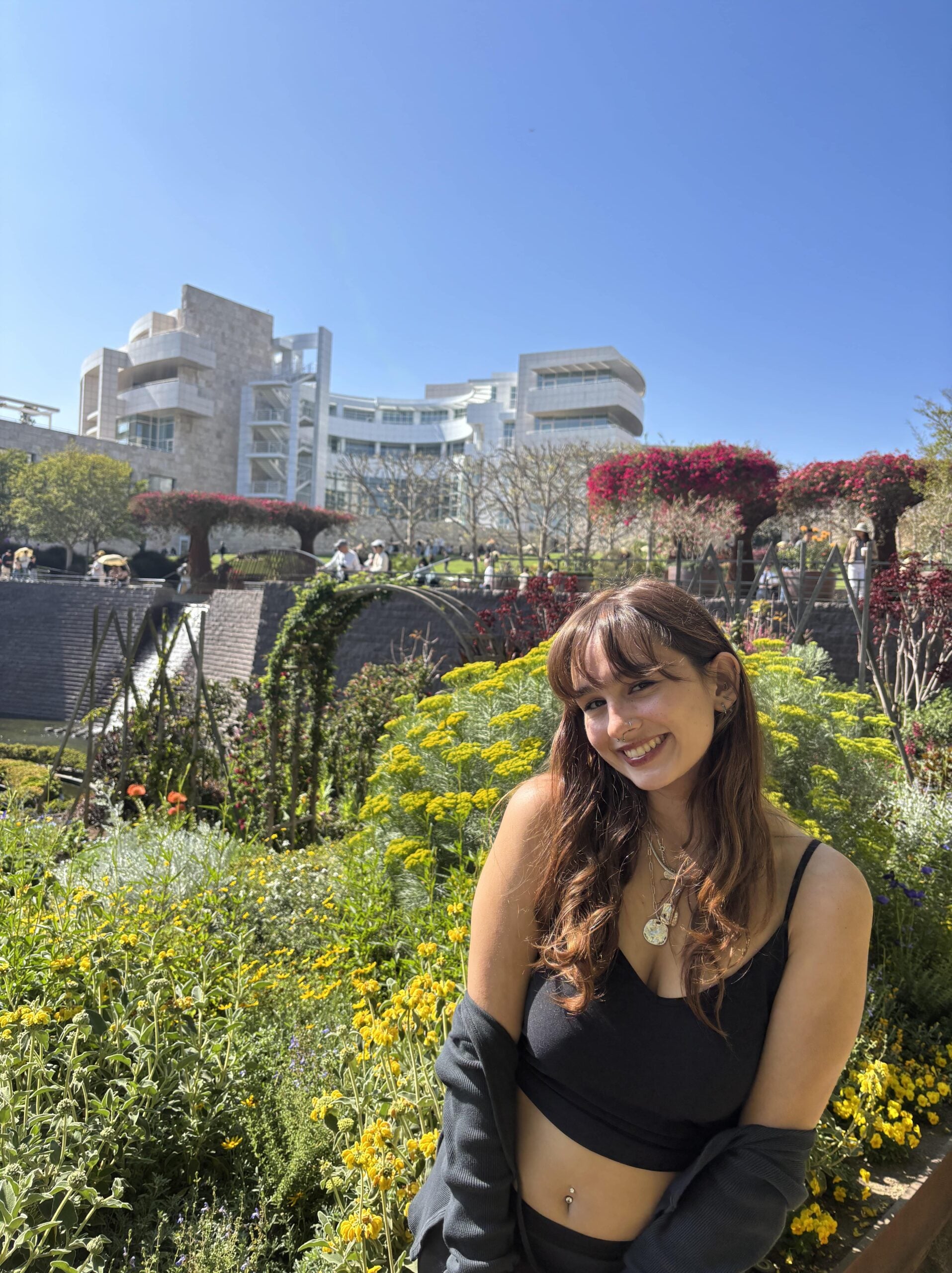 Cassandra Barron with brown wavy hair and bangs, wearing a black top, smiles in front of a flowery background. 