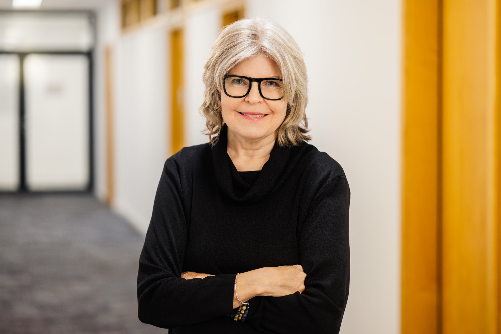 Kathryn Temple stands in a hallway with her arms crossed, smiling at the camera.