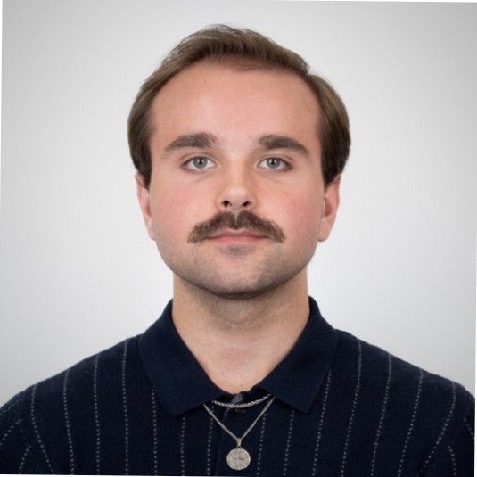 Benjamin Waida smiles softly at the camera in a black striped polo