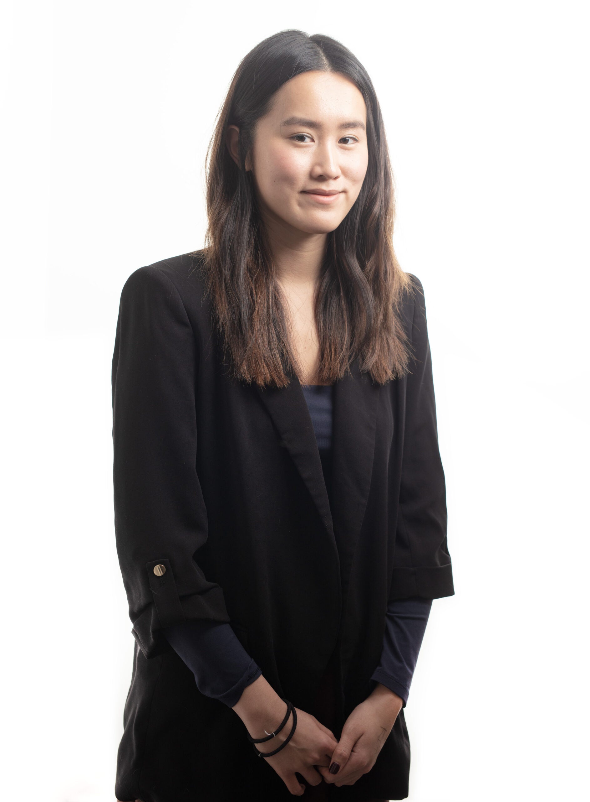 Amanda Chu stands in a black dress and jacket smiling softly at the camera