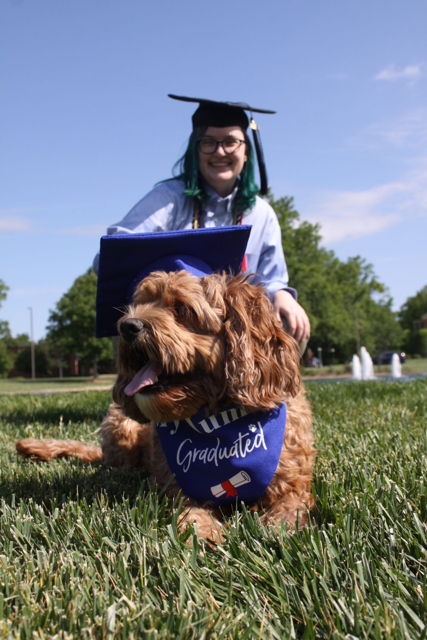 Cass All smiles in their graduation garb, a very cute dog in front of them with a cap and gown for its own!