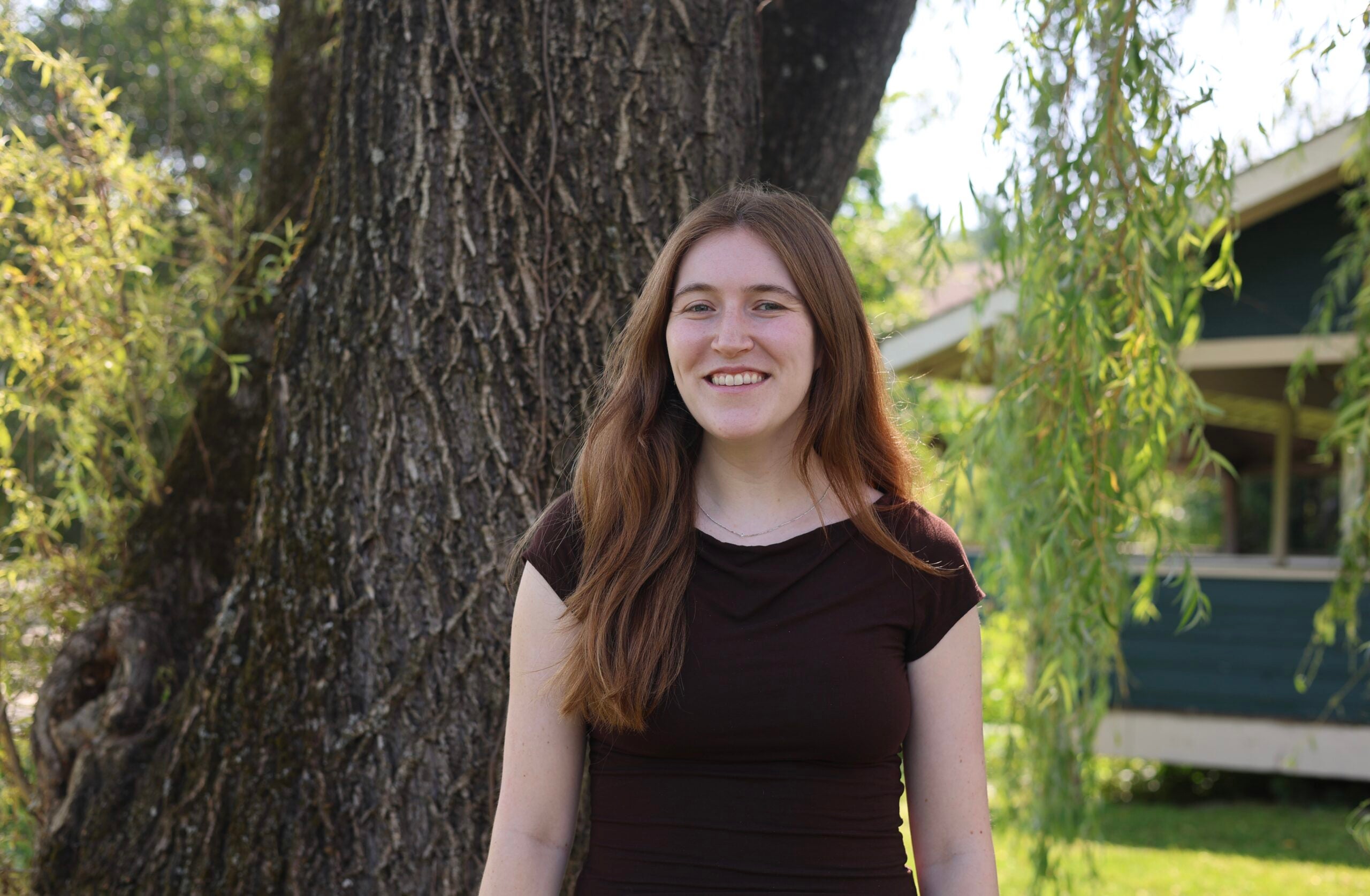 Laila Perlman smiles in fronit of a tree wearing a black dress.